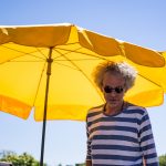 Man in a striped shirt in front of a yellow umbrella